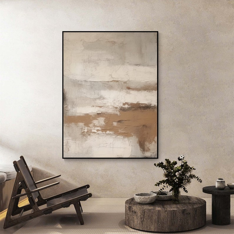 May include: Abstract painting in shades of brown, white, and gray. The painting is framed in a black frame and hangs on a light beige wall.