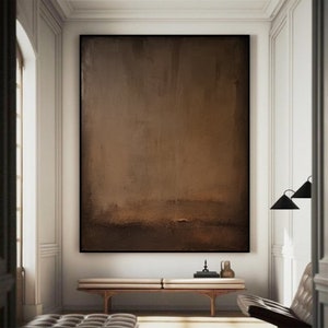 May include: Large abstract painting in shades of brown, with a black frame. The artwork hangs above a wooden bench in a well-lit room. The painting's color palette ranges from light to dark brown.
