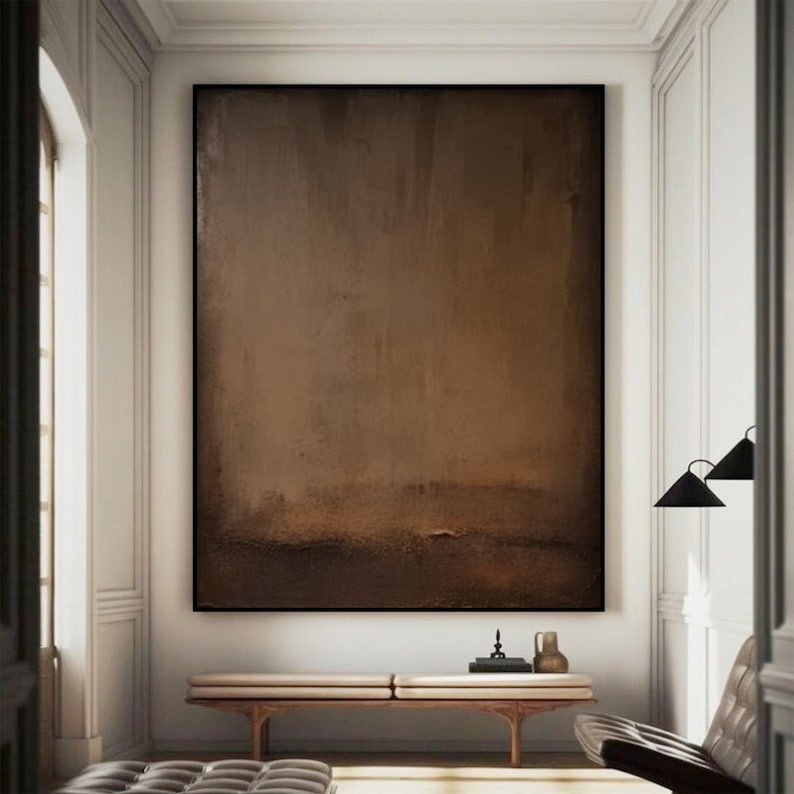 May include: Large abstract painting in shades of brown, with a black frame. The artwork hangs above a wooden bench in a well-lit room. The painting's color palette ranges from light to dark brown.