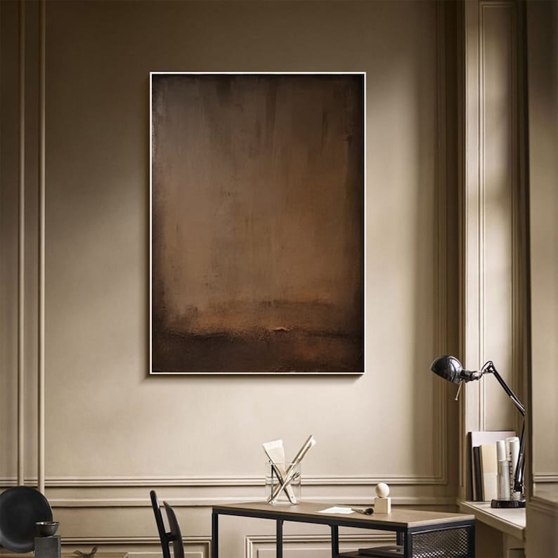 May include: Abstract art piece with a brown and tan color palette. The artwork is rectangular and framed in white, mounted on a neutral-toned wall. The painting has a textured appearance, with a gradient effect from top to bottom.