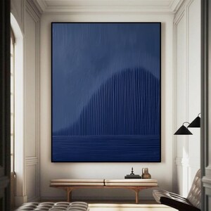 May include: Abstract painting with a blue background and vertical lines creating a wave-like shape. The painting is framed and hanging on a white wall.