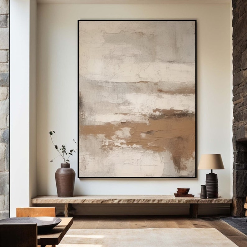 May include: Abstract painting with brown and white hues, featuring a textured, layered effect. The painting is framed in black and displayed on a wooden shelf above a brown rug.