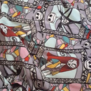 Puede incluir: Tela gris con un patr&oacute;n repetido de personajes de Pesadilla antes de Navidad. El dise&ntilde;o incluye la cara de Jack Skellington, Sally y otros elementos en un estilo de vidriera, con acentos de rojo, azul y amarillo.