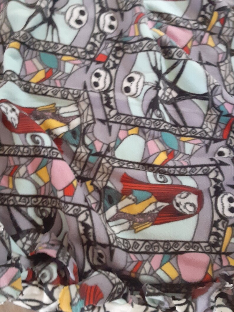 Puede incluir: Tela gris con un patr&oacute;n repetido de personajes de Pesadilla antes de Navidad. El dise&ntilde;o incluye la cara de Jack Skellington, Sally y otros elementos en un estilo de vidriera, con acentos de rojo, azul y amarillo.