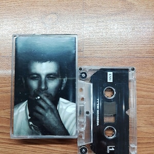 Könnte beinhalten: Eine transparente Kassette mit einem Schwarz-Weiß-Foto einer rauchenden Person. Daneben eine transparente Kassette mit schwarzem Innenraum und dem Text "PT. EMI INDONESIA".