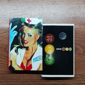 Puede incluir: Dos portadas de álbum de Blink-182. Una presenta a una mujer con uniforme de enfermera, la otra tiene el nombre de la banda y símbolos. La portada del álbum de la izquierda tiene el texto "blink-182".