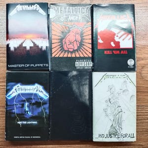 Op de afbeelding: Een verzameling van zes Metallica albumhoezen. De hoezen tonen albumtitels als "Master of Puppets", "St. Anger", "Kill 'Em All", "Ride the Lightning" en "...And Justice for All". De albumhoezen hebben verschillende ontwerpen en kleuren.