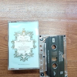 May include: A vintage cassette tape with a light blue cover featuring ornate gold detailing and the text "SINGLE COLLECTION." The cassette itself is black with white text, including "UTADA HIKARU" and "Single Collection Vol. 1."