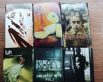 May include: Six Korn album covers are shown, each with unique artwork. The covers display a range of images, such as a teddy bear, a child's portrait, and abstract designs. The albums include "Follow the Leader," "Issues," "Untouchables," "Greatest Hits Vol. 1," and "Life is Peachy."