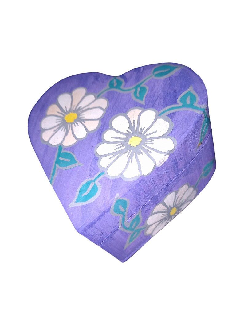 K&ouml;nnte beinhalten: Lilafarbener, herzf&ouml;rmiger Holzkasten mit Blumenmuster. Die Box ist mit wei&szlig;en G&auml;nsebl&uuml;mchen und gr&uuml;nen Bl&auml;ttern bemalt.