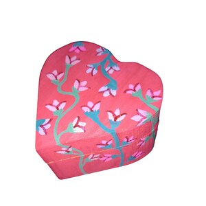 K&ouml;nnte beinhalten: Eine herzf&ouml;rmige Holzkiste, die in einem leuchtenden Pink mit einem floralen Design bemalt ist. Die Blumen sind rosa und wei&szlig; mit gr&uuml;nen Stielen.