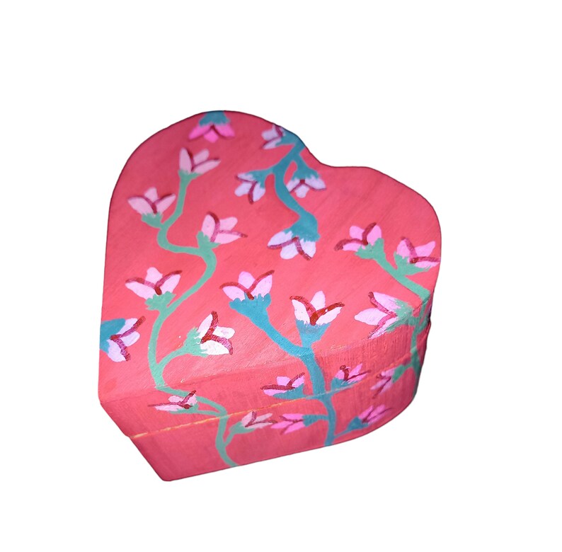 K&ouml;nnte beinhalten: Eine herzf&ouml;rmige Holzkiste, die in einem leuchtenden Pink mit einem floralen Design bemalt ist. Die Blumen sind rosa und wei&szlig; mit gr&uuml;nen Stielen.