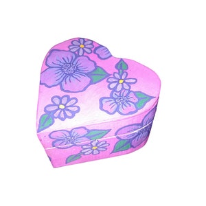 K&ouml;nnte beinhalten: Eine rosa herzf&ouml;rmige Schachtel mit einem Blumendesign. Die Blumen sind lila und blau mit gelben Zentren. Die Schachtel ist mit einem hellrosa Hintergrund bemalt.