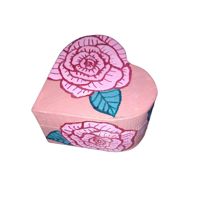 K&ouml;nnte beinhalten: Eine herzf&ouml;rmige Holzkiste, die rosa mit einem floralen Design bemalt ist. Die Kiste zeigt zwei rosa Rosen mit gr&uuml;nen Bl&auml;ttern.