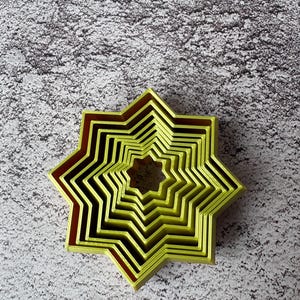 May include: A nested set of star-shaped cookie cutters in varying sizes. The cutters are a bright yellow-green color with a dark red-brown trim. The cutters are arranged in a nested pattern, with the smallest star in the center.