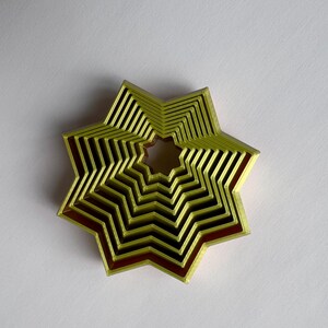 May include: A layered star-shaped object with a nested design. The object features a light green exterior with a dark red interior, creating a contrast. The star has multiple layers, giving it a three-dimensional appearance. The object is likely a decorative item.