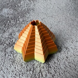 May include: A geometric, star-shaped decorative object with a stepped design. The object features a gradient of colors, transitioning from yellow-green at the base to orange at the top. The object is likely 3D-printed and has a unique, modern aesthetic.