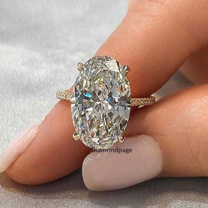 Könnte beinhalten: Ein goldener Verlobungsring mit einem großen ovalen Diamanten. Der Ring hat eine dünne Band mit kleinen Diamanten, die darin eingefasst sind.