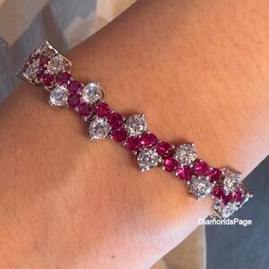 Könnte beinhalten: Ein schimmerndes Armband mit abwechselnden Clustern aus runden, brillant geschliffenen weißen Edelsteinen und leuchtenden, runden roten Edelsteinen. Das Armband ist in einem silberfarbenen Metall gefasst und für das Handgelenk konzipiert. Es ist ein Schmuckstück.