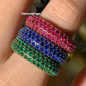 Peut inclure: Trois bagues colorées, serties de pavés, sont empilées sur un doigt. Les bagues sont de couleurs verte, bleue et rose. Les bagues sont composées de petites pierres précieuses rondes. Un accessoire vibrant et accrocheur.