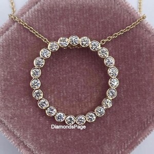 Puede incluir: Un collar dorado con un colgante circular engastado con numerosas piedras preciosas transparentes. El collar se exhibe sobre una superficie de terciopelo rosa. El texto "DiamondsPage" es visible.
