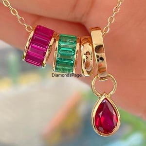 May include: A gold necklace featuring a pendant with a red teardrop-shaped gemstone. The necklace also includes three gold rings, one with a row of pink gemstones, one with green gemstones, and one plain gold ring.
