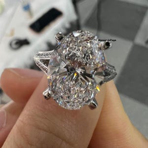 Puede incluir: Un anillo de compromiso de diamante de forma ovalada con engaste pavé. El anillo está engastado en oro blanco y presenta un diseño delicado e intrincado.