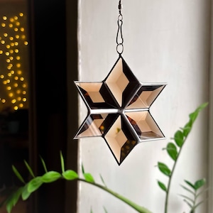 Könnte beinhalten: Ein brauner Glasstern aus Buntglas mit einer silbernen Kette, die oben hängt.