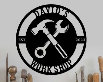 May include: Black and white metal sign with the text "David's Workshop" in a circle. The sign also includes a hammer and wrench crossed over each other, the text "EST" and "2023", and a white background.