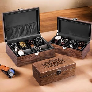May include: Two wooden watch boxes with a personalised engraved box. The larger box has a black interior and holds eight watches. The smaller box has a brown interior and is engraved with the name "WILSON".