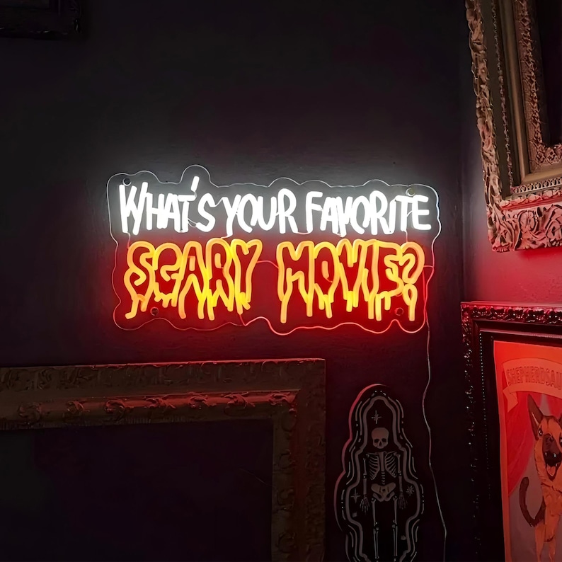 Peut inclure: Un panneau lumineux au n&eacute;on avec le texte "Quel est votre film d'horreur pr&eacute;f&eacute;r&eacute; ?" en lettres blanches et orange. Le panneau est mont&eacute; sur un mur sombre.