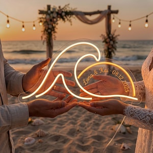 May include: A clear acrylic sign featuring a glowing warm yellow neon wave design. The sign is personalized with the text Luna & Kai and the date 08.12.2025 etched in a cursive font within the wave shape, creating a bright decorative display.