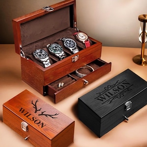 Könnte beinhalten: Zwei Holzuhrenboxen mit einer Schublade. Die obere Box hat eine dunkelbraune Oberfläche und ist geöffnet, wodurch fünf Uhrenschlitze sichtbar werden. Die untere Box hat eine hellbraune Oberfläche und ist geschlossen. Beide Boxen haben den Namen "WILSON" auf der Vorderseite eingraviert.