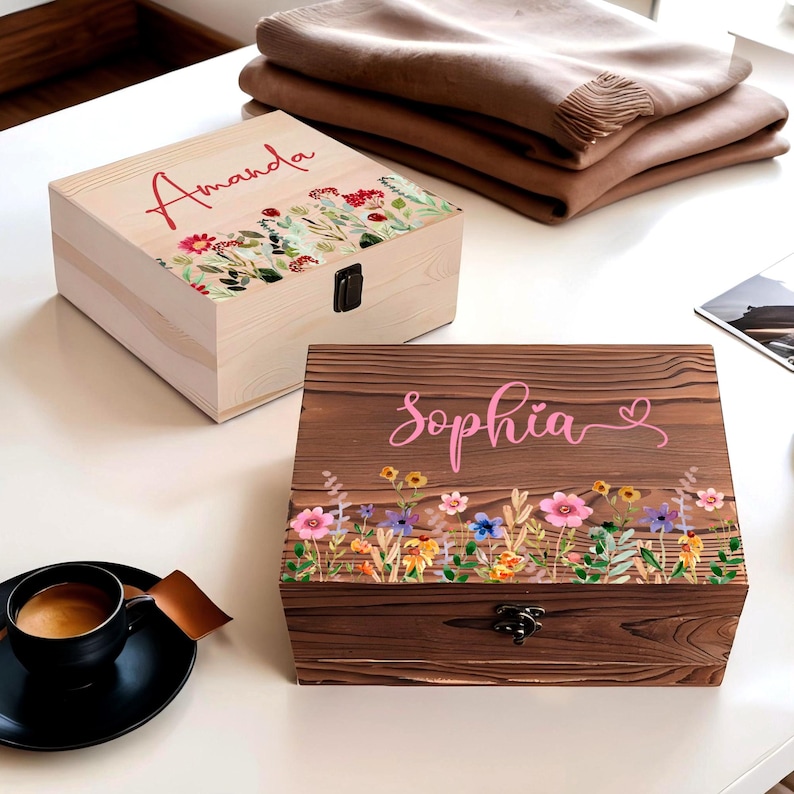 May include: Two wooden keepsake boxes, one light-colored and one dark-colored, with floral designs. The light box has the name "Amanda" in red script. The dark box has the name "Sophia" in pink script. Both have metal clasps.