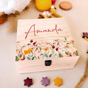 May include: Wooden keepsake box with the name "Amanda" in red script. The box features a watercolor floral design with yellow, orange, and red flowers. A black clasp secures the box. Three star-shaped decorations are at the bottom.