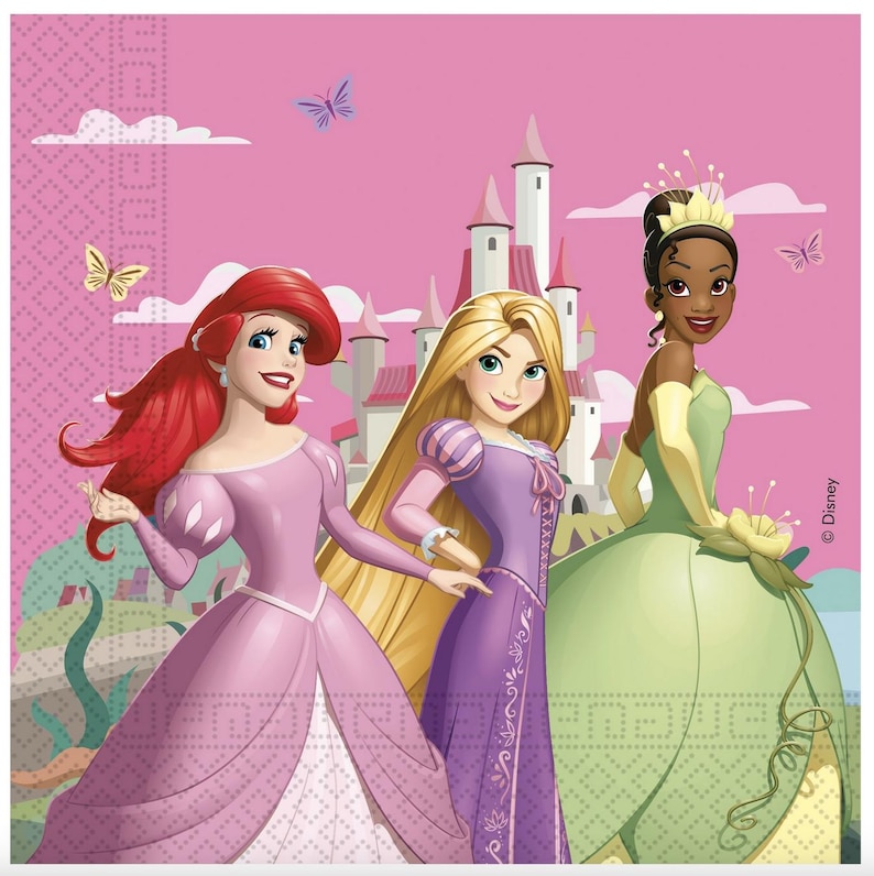 May include: A square paper napkin featuring three animated princesses against a pink castle background. The left figure has long red hair and a pink gown, the center figure has long blonde hair and a purple dress, and the right figure wears a green gown.