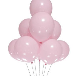 May include: A cluster of nine round, light pink balloons arranged in a pyramid shape. Each balloon has a smooth, matte finish and is attached to a thin, silver-colored string. The balloons are inflated to a uniform size and are grouped together.