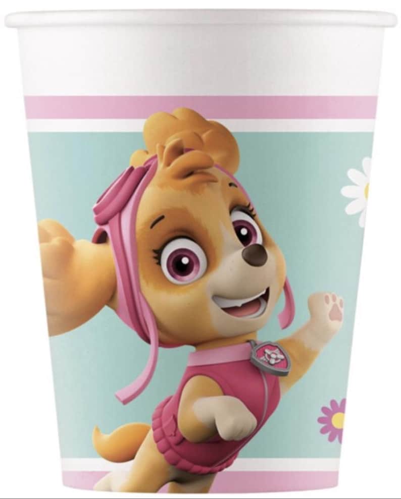 May include: A white paper cup featuring a cartoon image of Skye from Paw Patrol. The cup has a light blue background with pink and white stripes. Skye is depicted in a pink outfit with a happy expression.