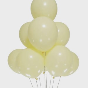 May include: A cluster of nine round, pale yellow balloons arranged in a pyramid shape. Each balloon has a smooth, matte finish and is attached to a thin, silver-colored string. The balloons are uniform in color and size, creating a cohesive group.