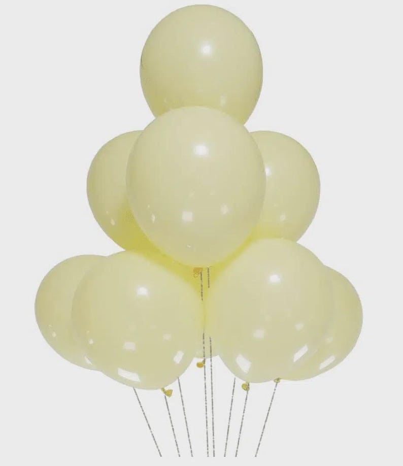 May include: A cluster of nine round, pale yellow balloons arranged in a pyramid shape. Each balloon has a smooth, matte finish and is attached to a thin, silver-colored string. The balloons are uniform in color and size, creating a cohesive group.
