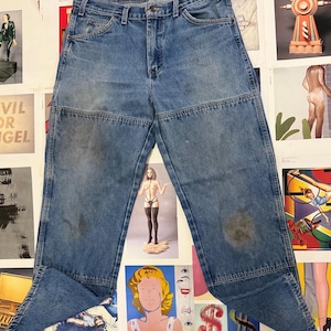 May include: Light blue denim jeans with a unique design featuring reinforced knee panels. The jeans have a classic five-pocket design and a button and zipper closure. The denim shows signs of wear, adding to its vintage appeal.