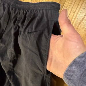 May include: Black athletic pants with an elastic waistband and a small Nike logo. The pants have a pocket and are made of a lightweight material.