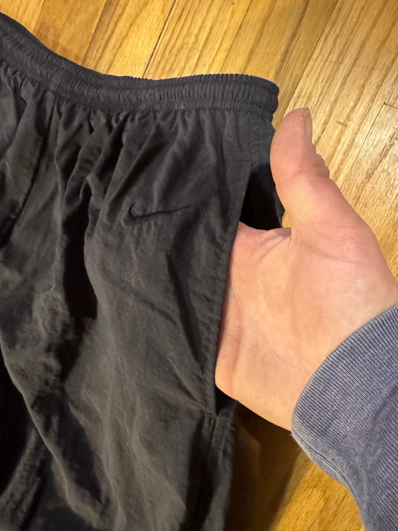 May include: Black athletic pants with an elastic waistband and a small Nike logo. The pants have a pocket and are made of a lightweight material.