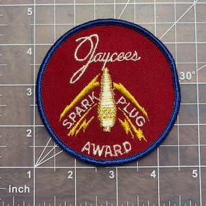 May include: A red and blue circular patch with the text "Jaycees SPARK PLUG AWARD" in gold lettering. The patch features a stylized spark plug in the center.