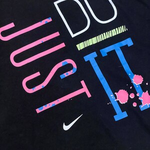 May include: Black t-shirt with the text "Just Do It" in pink, blue, and white. The text is stylized with paint splatters and a Nike swoosh logo.