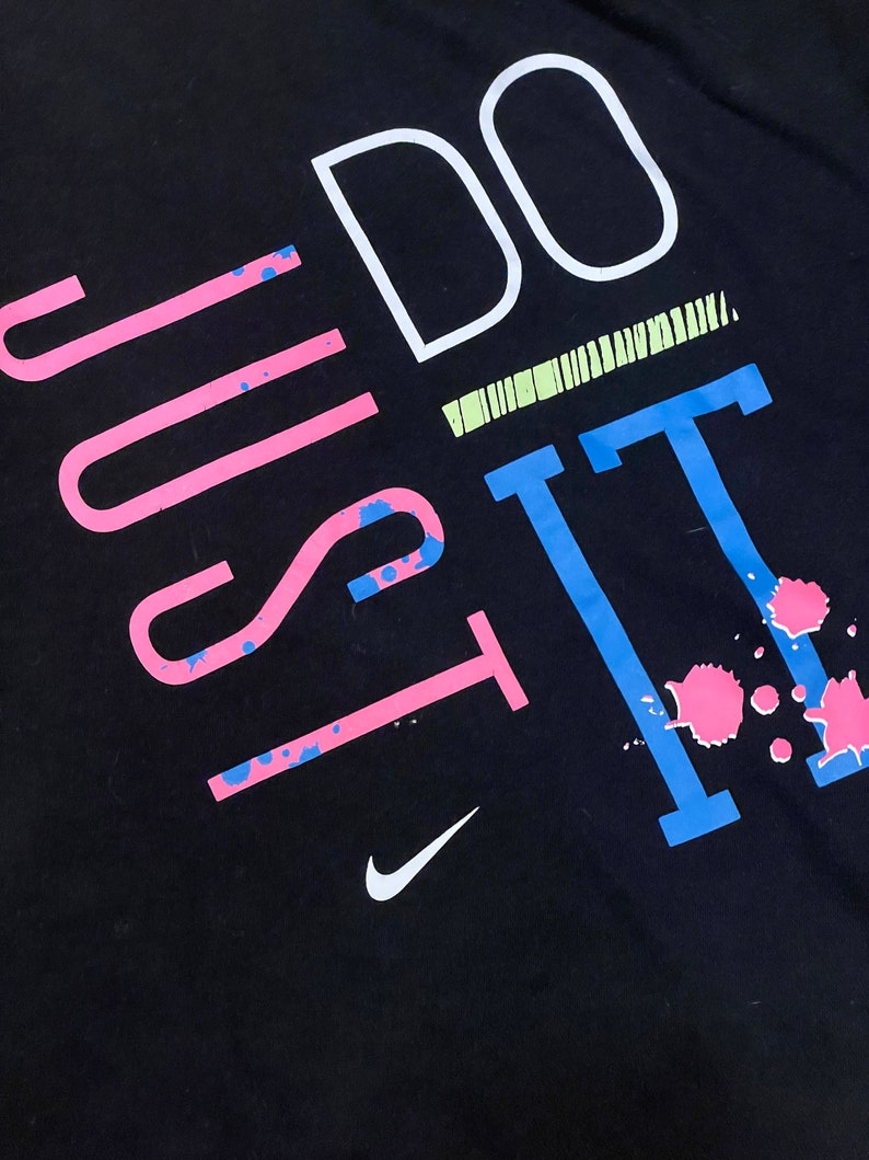 May include: Black t-shirt with the text "Just Do It" in pink, blue, and white. The text is stylized with paint splatters and a Nike swoosh logo.