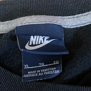 May include: Black Nike sweatshirt with a white Nike logo and a black tag that says "XL TG EG MADE IN PAKISTAN FABRIQUE AU PAKISTAN".