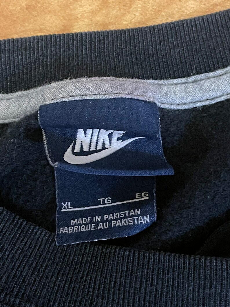 May include: Black Nike sweatshirt with a white Nike logo and a black tag that says "XL TG EG MADE IN PAKISTAN FABRIQUE AU PAKISTAN".
