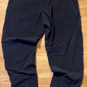 May include: Black athletic pants with an elastic waistband. The pants are made of a lightweight material and have a relaxed fit. The pants are suitable for various activities, including running, yoga, or casual wear.