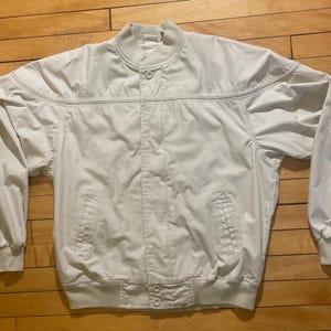 May include: A light beige bomber jacket with a zipper closure and a ribbed collar. The jacket has two pockets on the front and a ribbed hem.